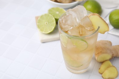 Photo of Glass of tasty ginger ale with ice cubes and ingredients on white tiled table, closeup. Space for text
