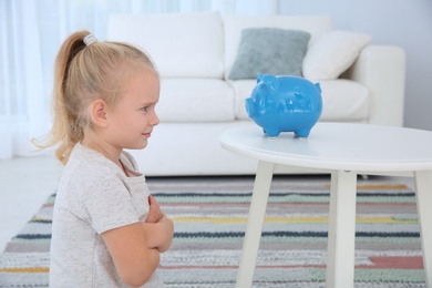 Emotional little girl with piggy bank at home