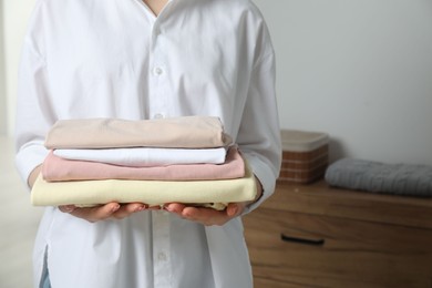 Woman holding folded clothes at home, closeup. Space for text