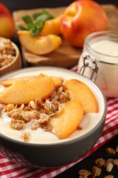 Photo of Tasty peach yogurt with granola and pieces of fruits in bowl on table