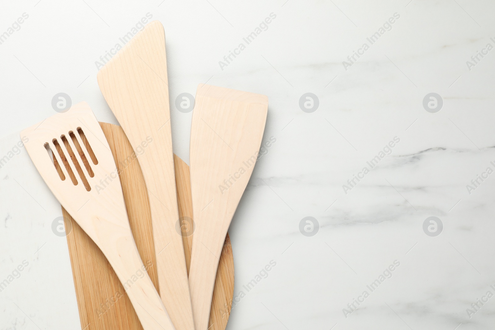 Photo of Board with different wooden spatulas on light marble table, top view. Space for text