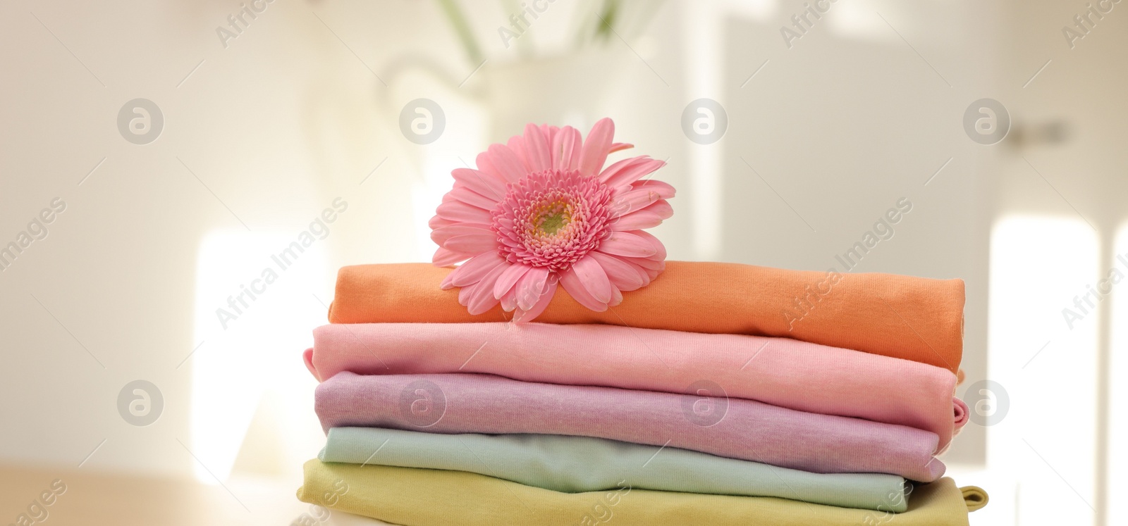 Photo of Stack of clean clothes and pink flower on wooden table