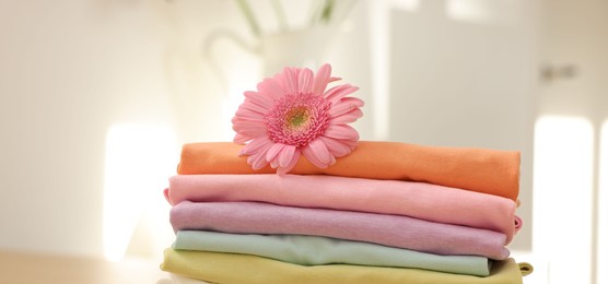 Photo of Stack of clean clothes and pink flower on wooden table