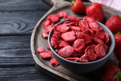 Photo of Freeze dried and fresh strawberries on black wooden table, closeup. Space for text