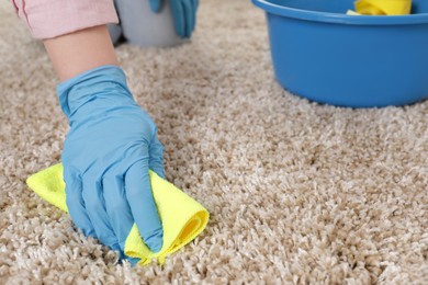 Woman in rubber gloves cleaning carpet with rag indoors, closeup. Space for text