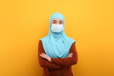 Portrait of Muslim woman in hijab and medical mask on orange background