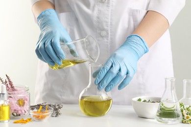 Photo of Scientist developing cosmetic oil at white table, closeup