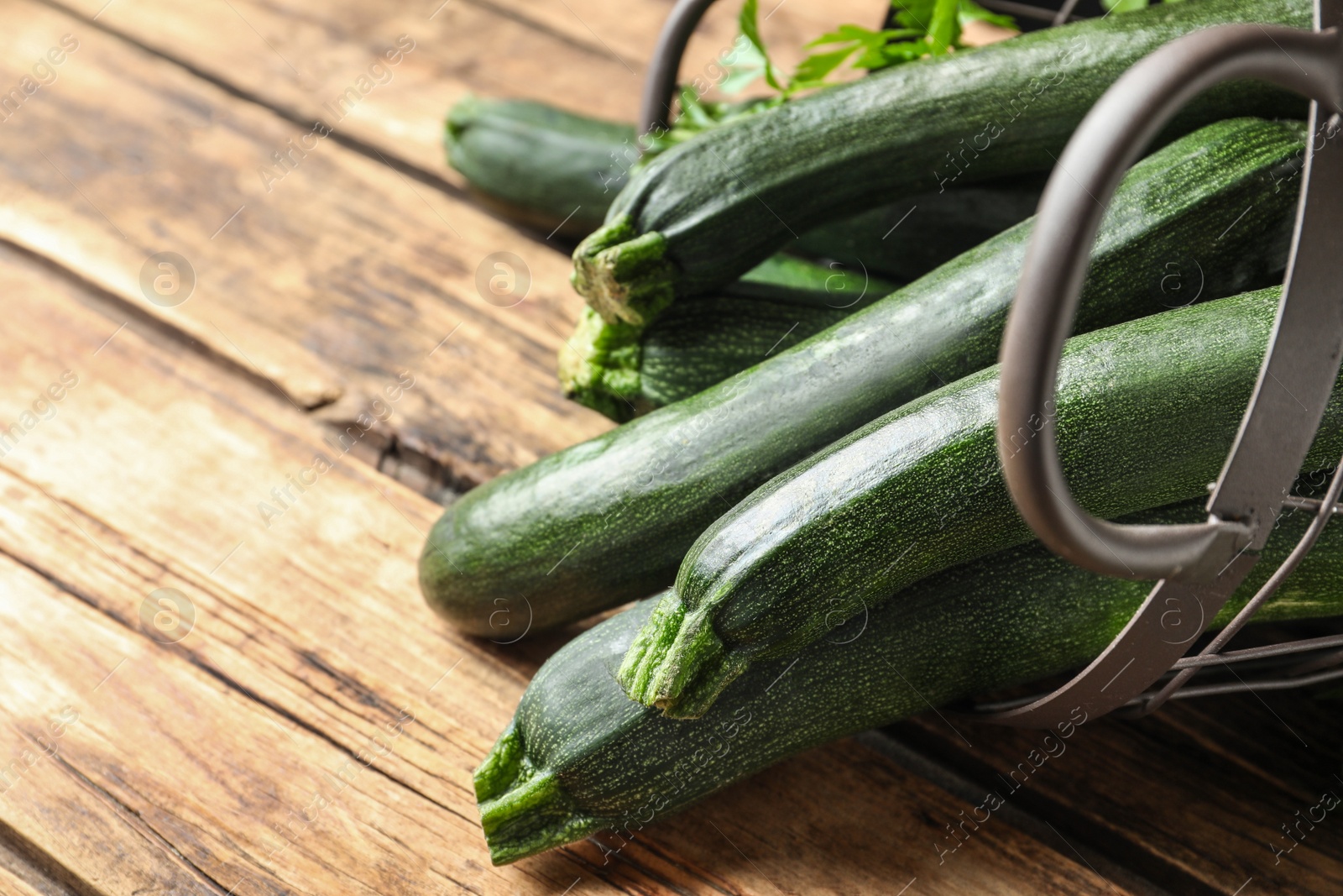 Photo of Basket with green zucchinis on wooden table, closeup