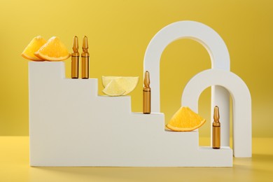 Stylish presentation of skincare ampoules with vitamin C and citrus slices on yellow background