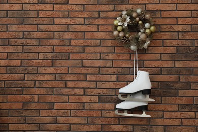 Pair of ice skates and beautiful Christmas wreath hanging on brick wall, space for text