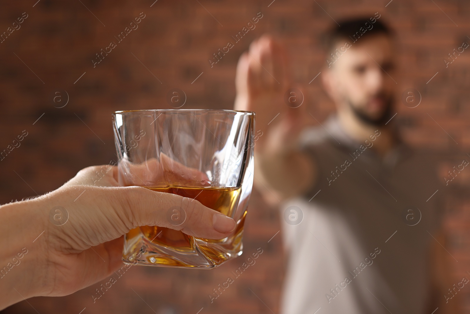 Photo of Man refusing to drink whiskey near red brick wall, closeup. Alcohol addiction treatment