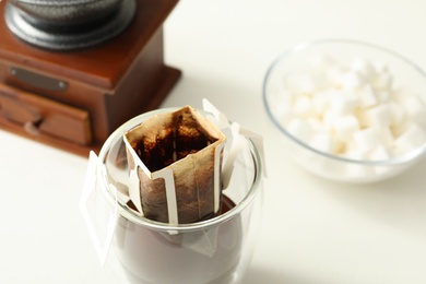Photo of Glass with drip coffee bag on white table, closeup