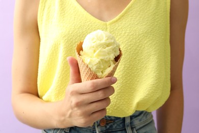 Photo of Woman holding yellow ice cream in wafer cone on violet background, closeup