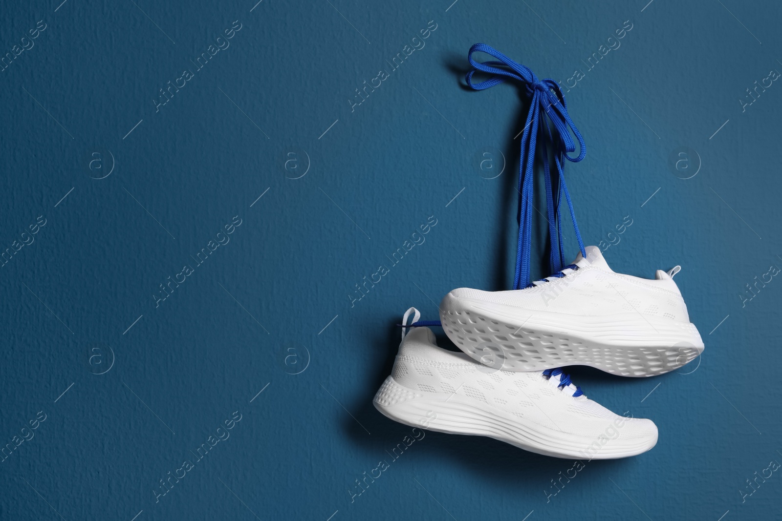 Photo of Pair of stylish shoes with laces hanging on blue wall, space for text