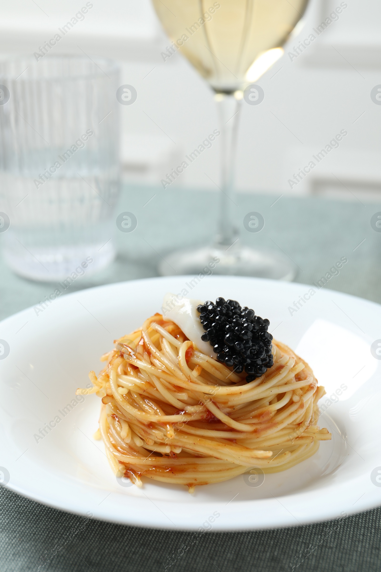 Photo of Tasty spaghetti with tomato sauce and black caviar served on table, closeup. Exquisite presentation of pasta dish