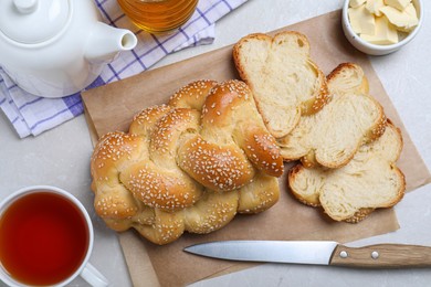Photo of Cut homemade braided bread and freshly brewed tea on light grey table, flat lay. Traditional Shabbat challah