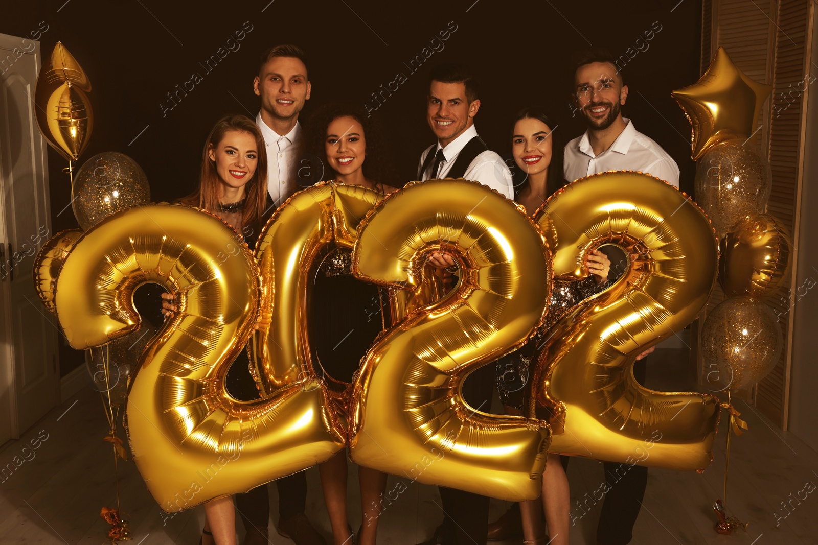 Photo of Happy friends with golden 2022 balloons indoors. New Year celebration