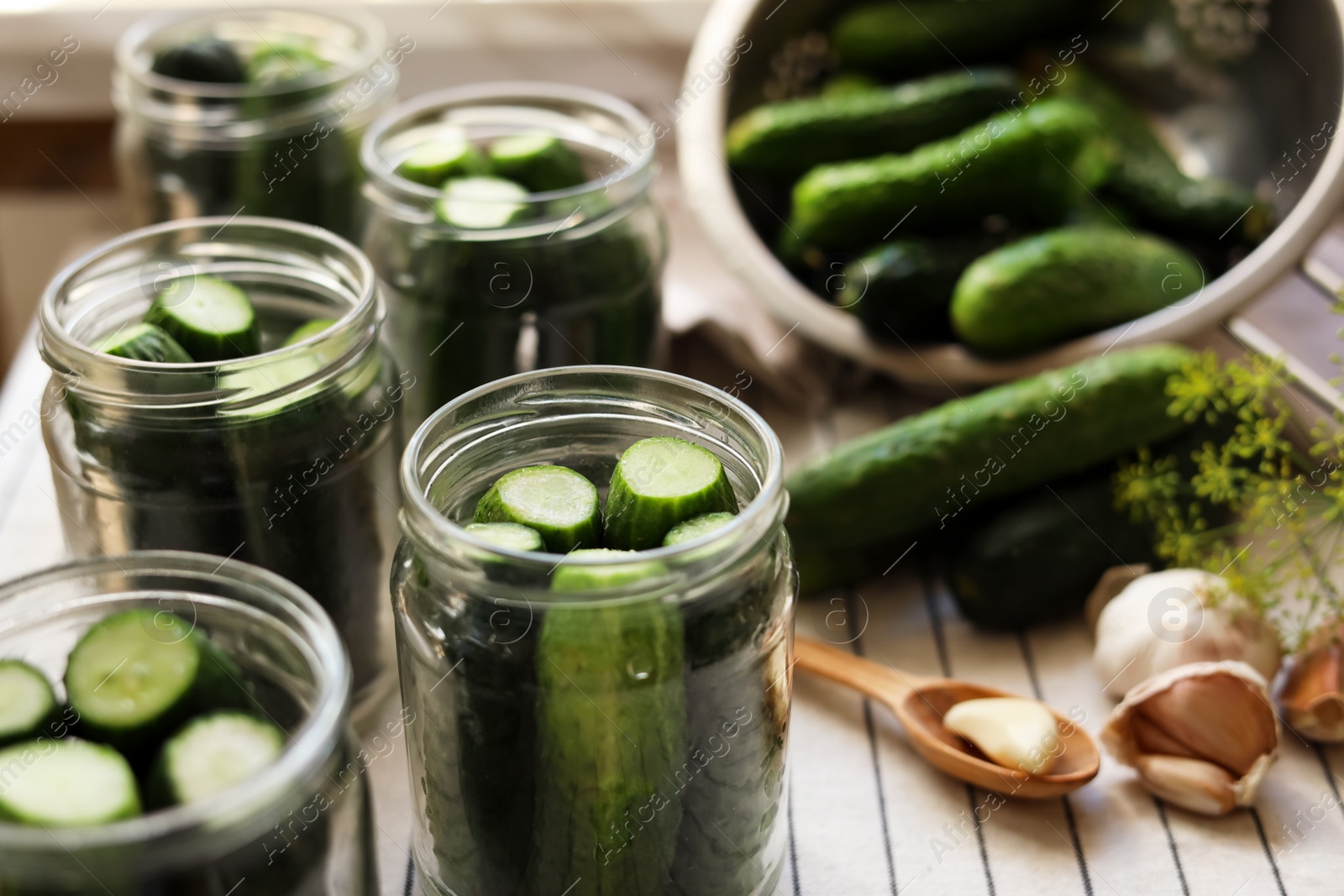 Photo of Glass jars with fresh cucumbers and other ingredients on table, closeup. Canning vegetables