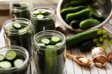 Glass jars with fresh cucumbers and other ingredients on table, closeup. Canning vegetables