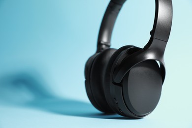 Photo of Modern wireless headphones on light blue background, closeup. Space for text