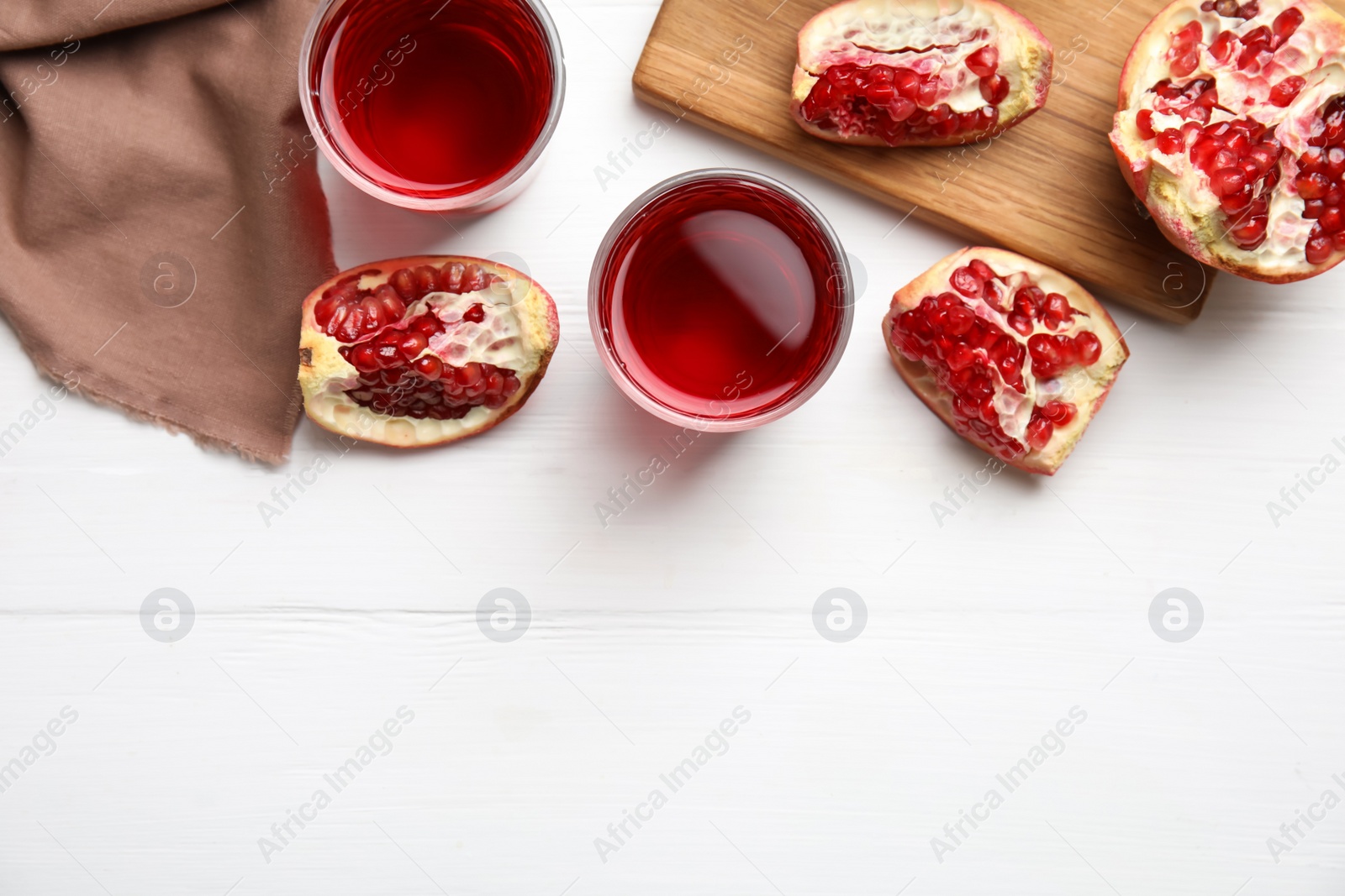 Photo of Glasses of pomegranate juice on white wooden table, flat lay. Space for text