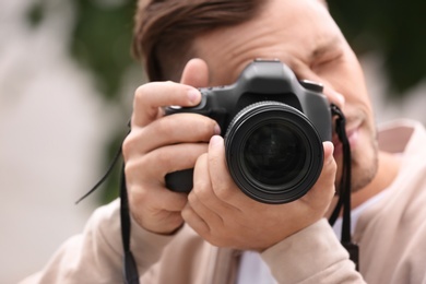 Male photographer with professional camera on blurred background, closeup