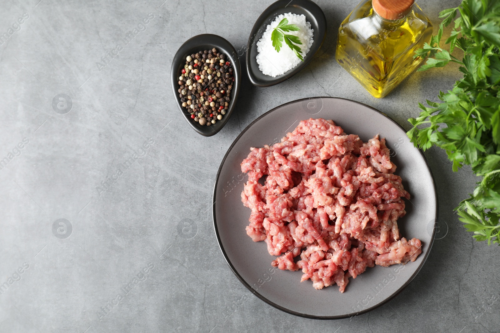 Photo of Raw ground meat, spices, parsley and oil on grey table, flat lay. Space for text