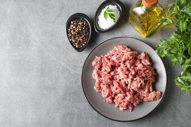 Photo of Raw ground meat, spices, parsley and oil on grey table, flat lay. Space for text