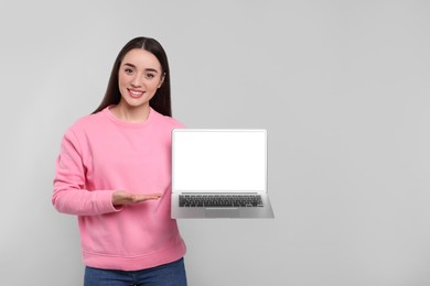 Smiling young woman with laptop on grey background, space for text