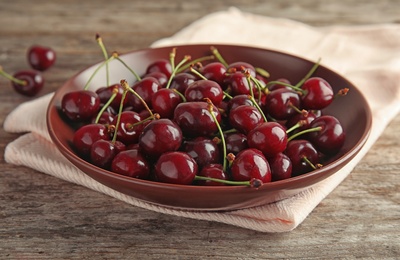 Photo of Plate with sweet red cherries on wooden table