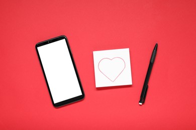 Photo of Long-distance relationship concept. Smartphone, love note and pen on red background, flat lay