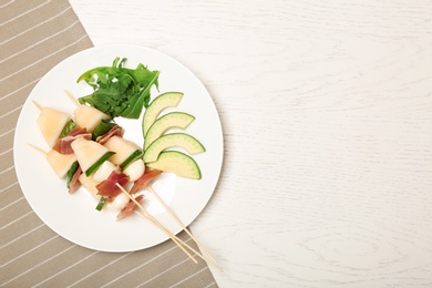 Plate with melon, mozzarella and prosciutto skewers on table, top view. Space for text