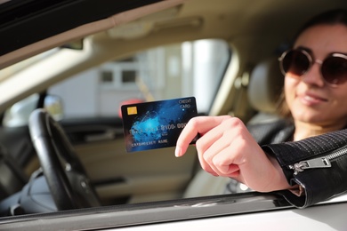 Woman sitting in car and giving credit card at gas station, closeup