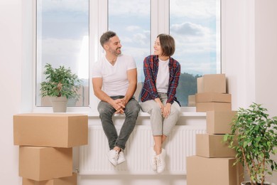 Photo of Happy couple sitting on windowsill in new apartment. Moving day