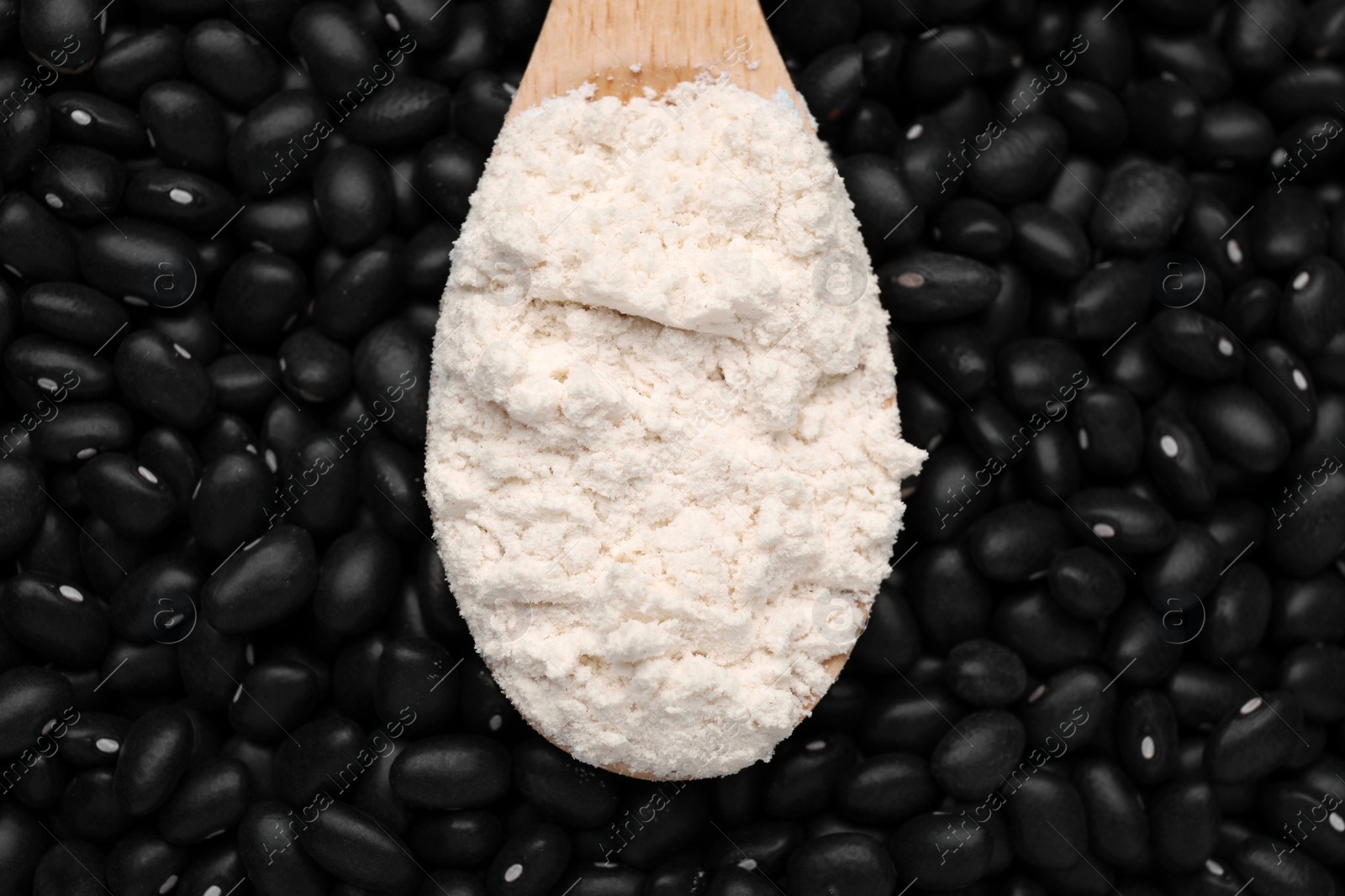 Photo of Wooden spoon with flour on black kidney beans, top view