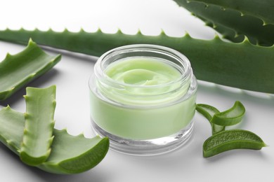 Photo of Jar of natural cream and aloe leaves on white background, closeup