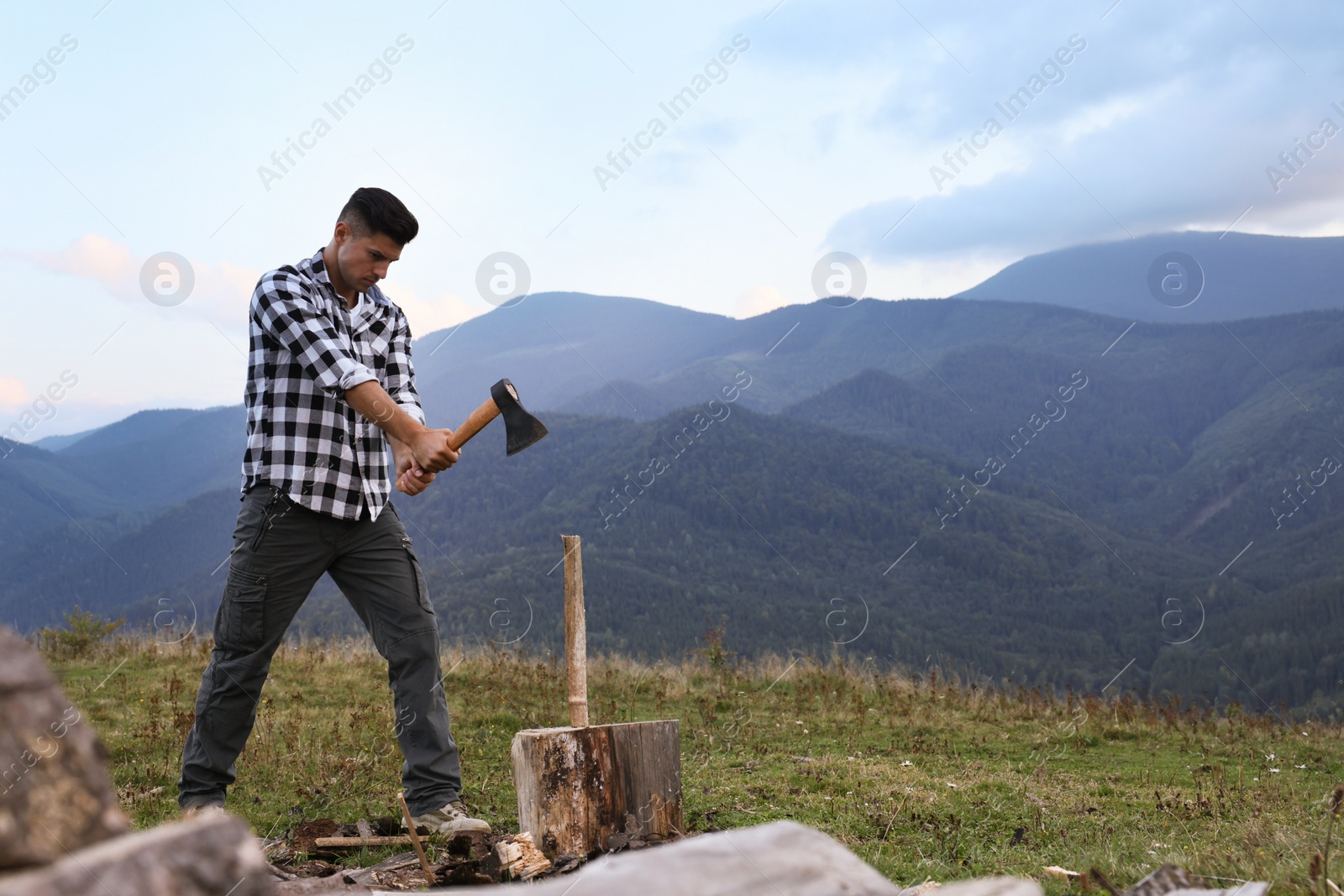 Photo of Handsome man with axe cutting firewood in mountains