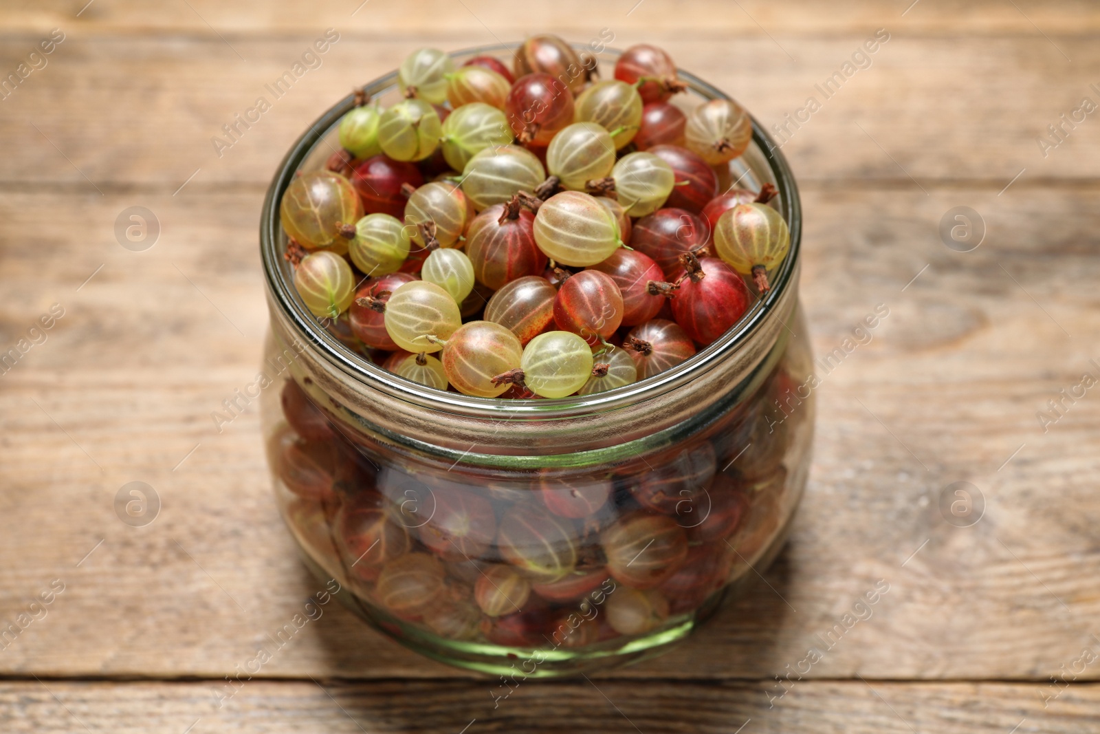Photo of Jar of fresh ripe gooseberries on wooden table, closeup