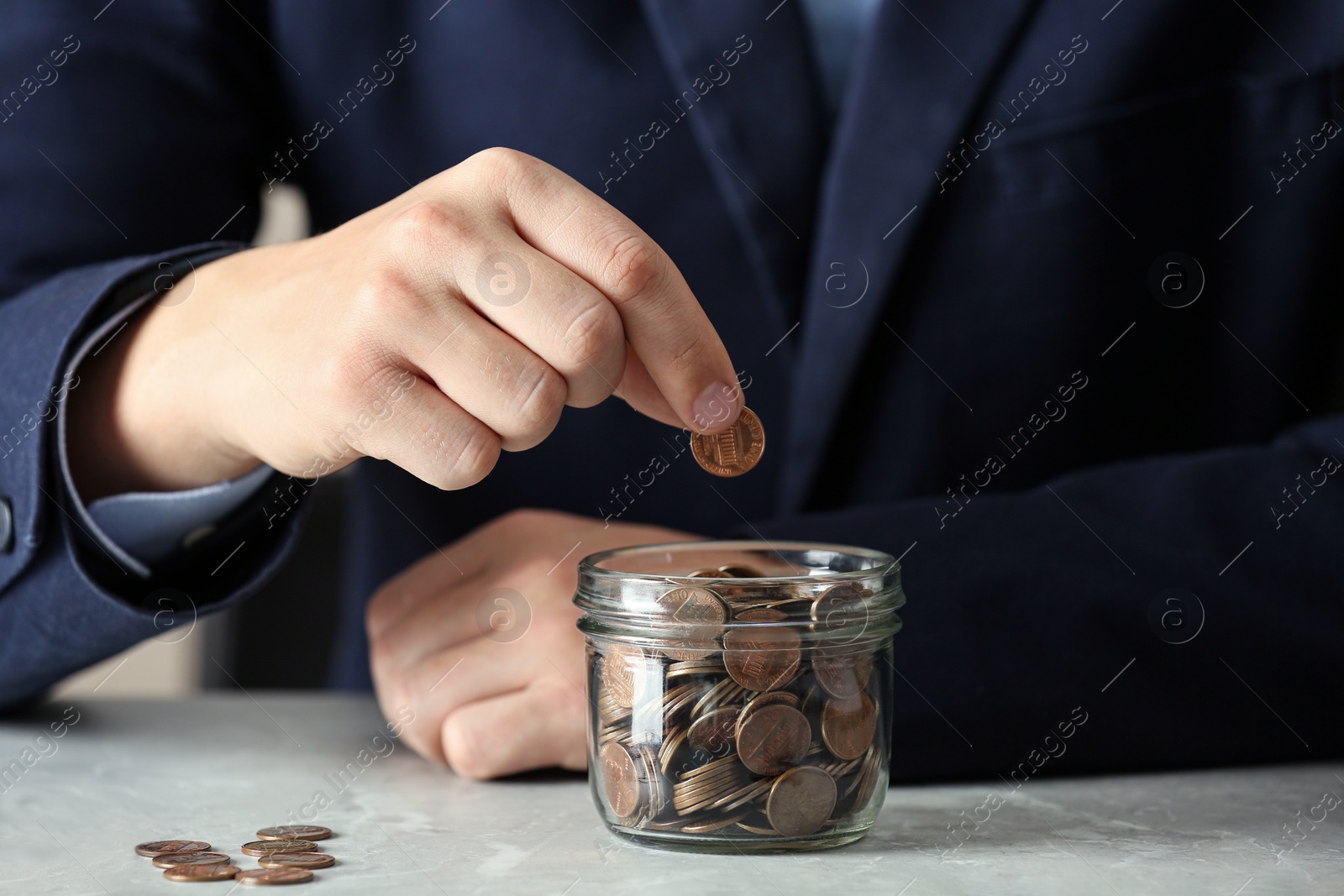 Photo of Man putting coin into jar at grey marble table, closeup. Money savings