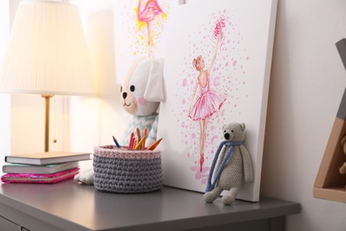 Picture and stationery with toys on chest of drawers in children's room. Interior design