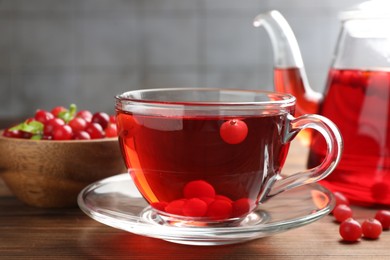 Photo of Tasty hot cranberry tea in glass cup and fresh berries on wooden table