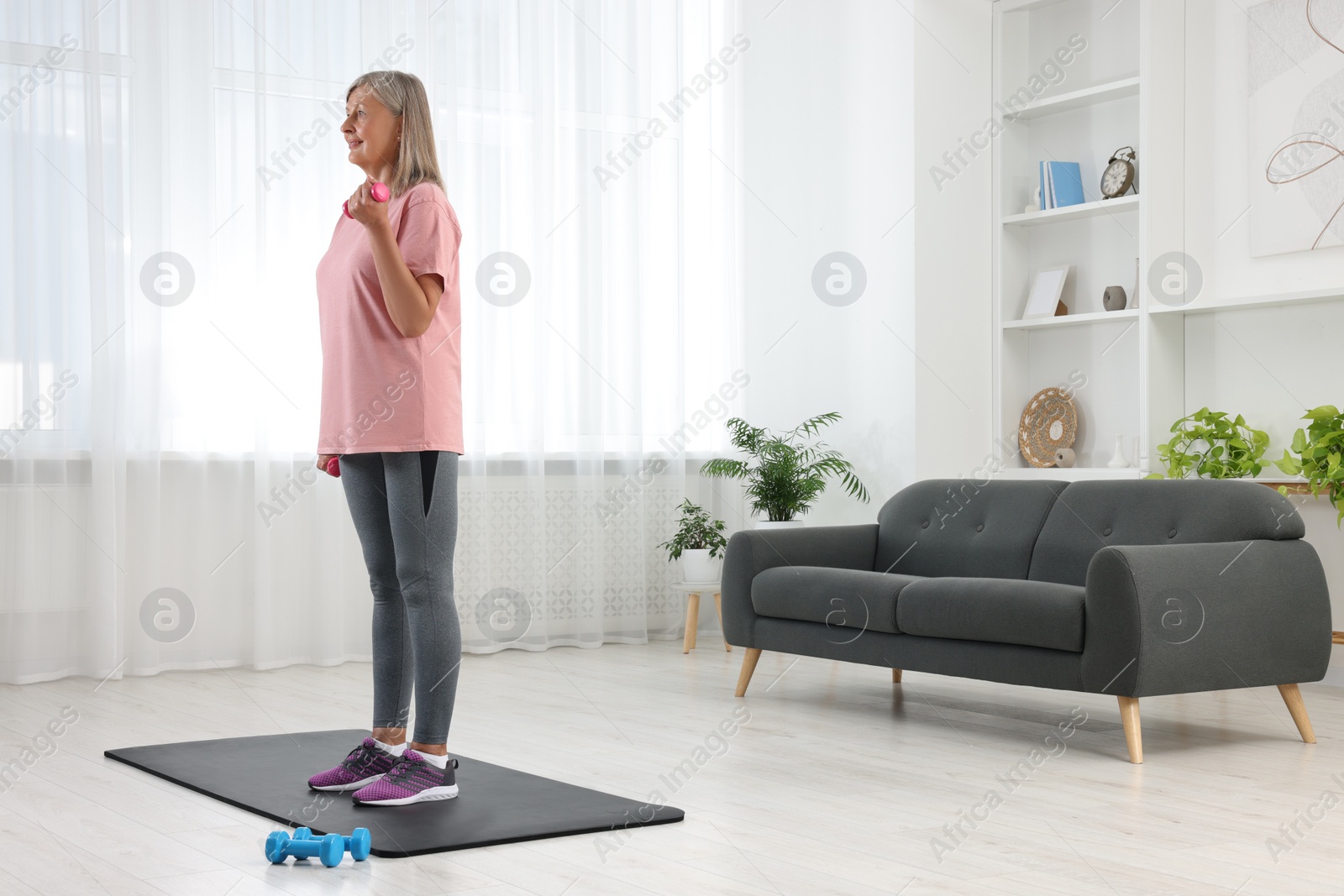 Photo of Senior woman exercising with dumbbells on mat at home. Sports equipment