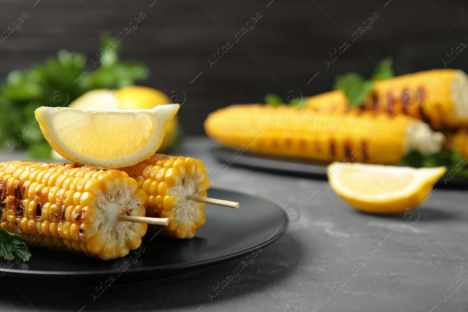 Photo of Plate of grilled corn cobs and lemon on grey table, closeup. Space for text