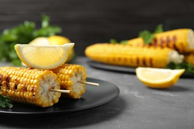 Photo of Plate of grilled corn cobs and lemon on grey table, closeup. Space for text