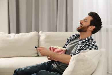 Photo of Laughing man watching TV with popcorn on sofa at home