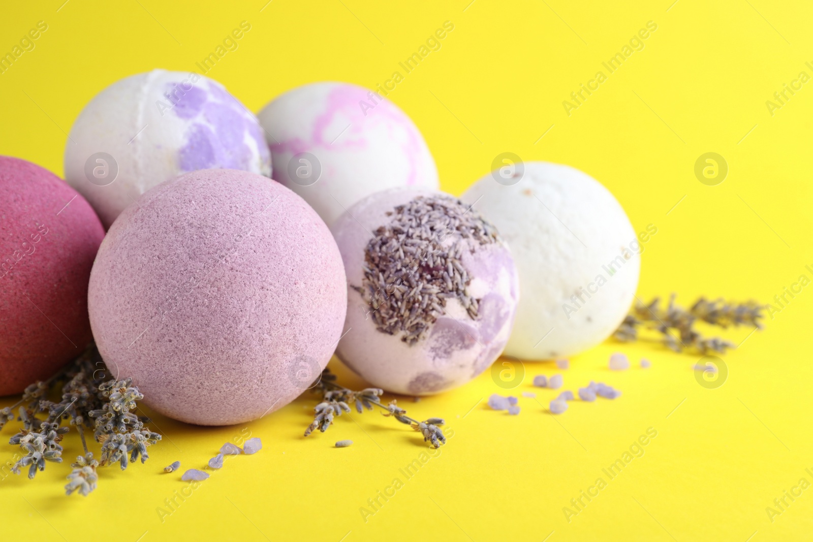 Photo of Colorful bath bombs, salt and dried lavender on yellow background, closeup