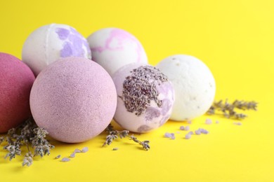 Photo of Colorful bath bombs, salt and dried lavender on yellow background, closeup