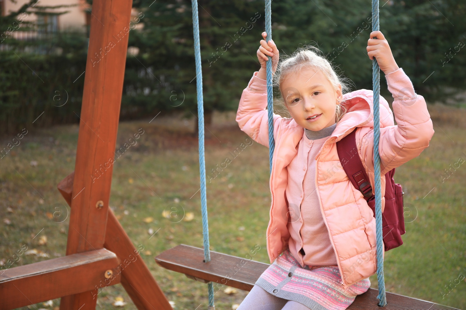 Photo of Cute little girl with backpack on swing outdoors