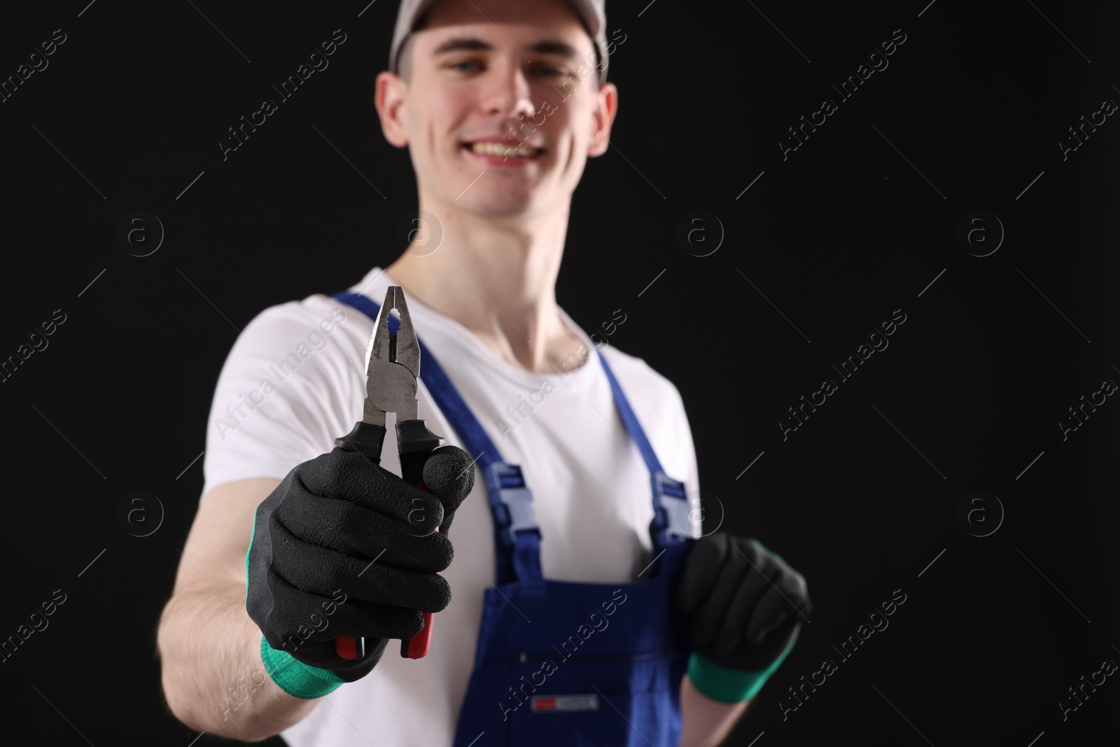 Photo of Young man holding pliers on black background, selective focus. Space for text