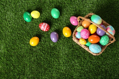 Photo of Wicker basket with Easter eggs on green grass, flat lay. Space for text